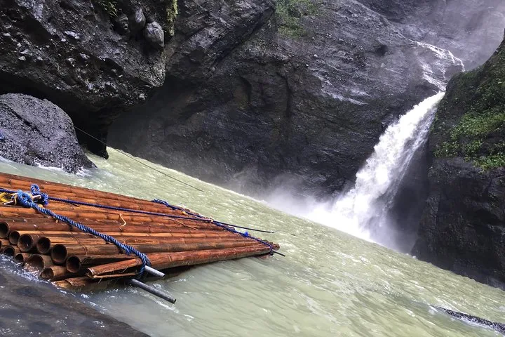 Empty bamboo raft floating in river water near a rushing waterfall