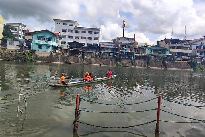 Pequeño bote con pasajeros avanzando por un río que pasa junto a edificios del pueblo